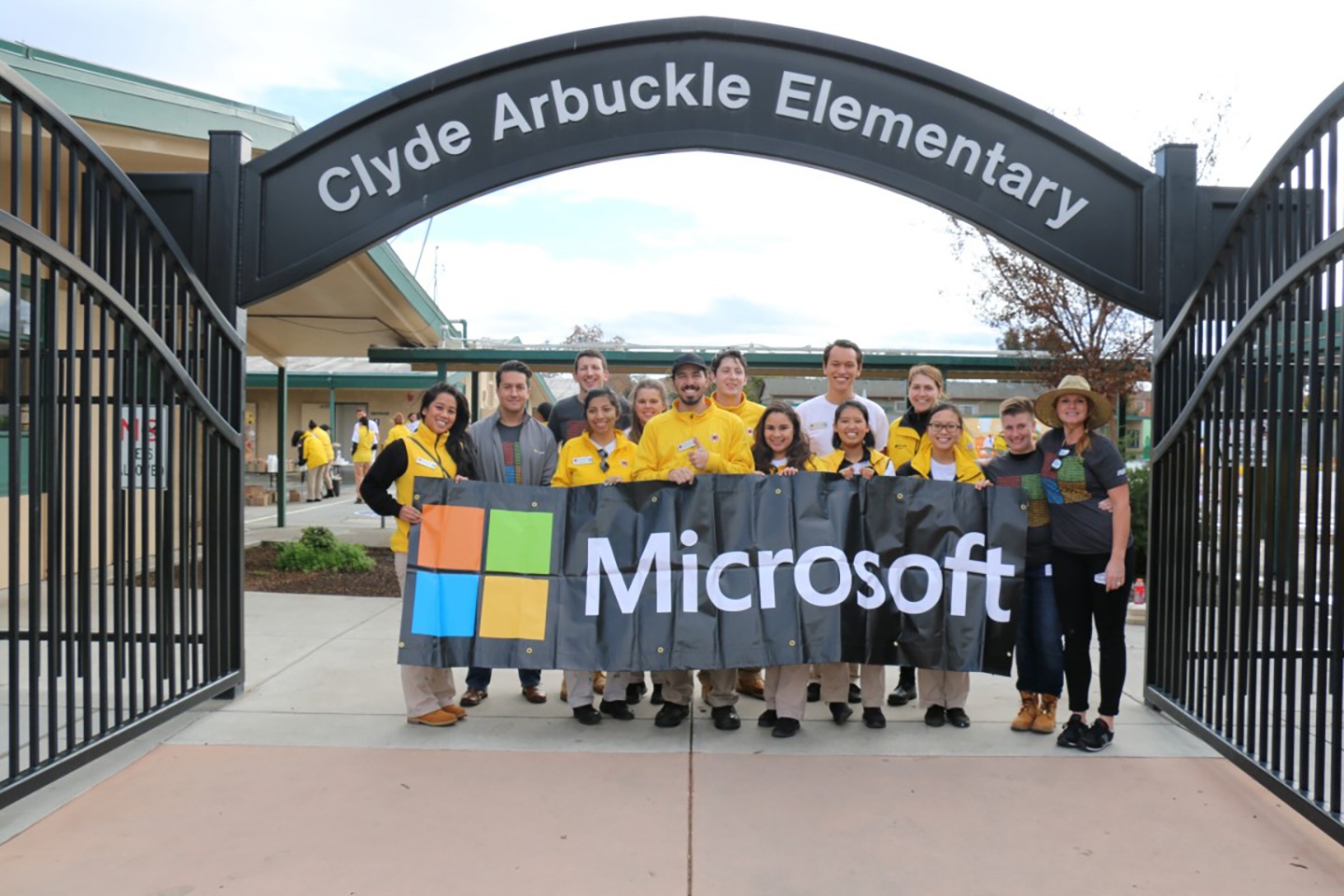Group of AmeriCorps members holding a large Microsoft banner in front of a school team sponsor