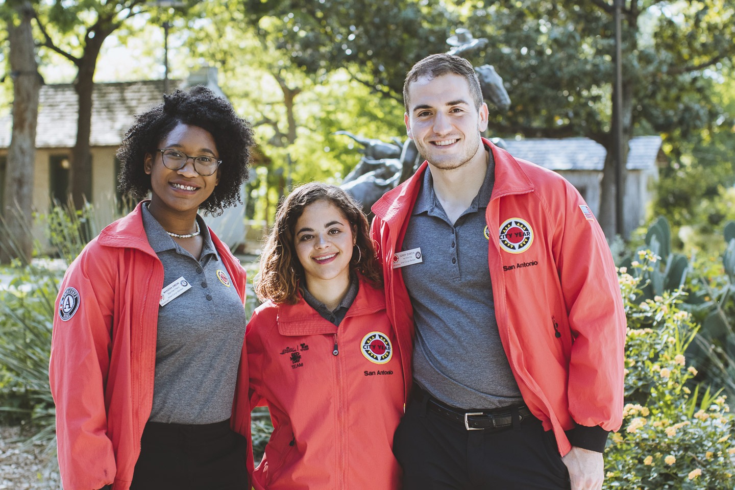 3 AmeriCorps members smile at the camera wearing their red City Year jackets