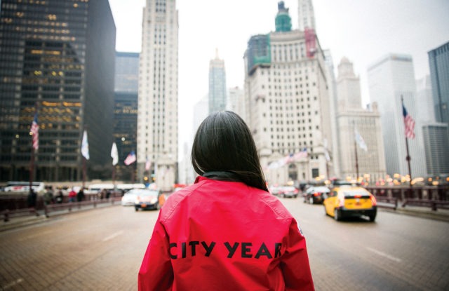 AmeriCorps member stands on a busy street looking up at the city.