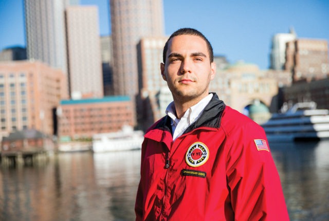 AmeriCorps member stands in front of the city skyline and water.