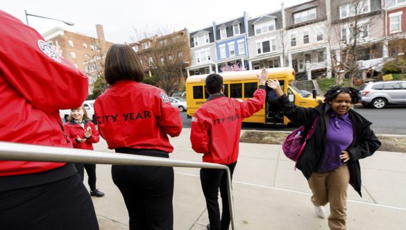 As students exit the school bus they find a team of City Year AmeriCorps members lined up to welcome them to school
