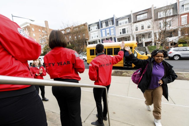 As students exit the school bus they find a team of City Year AmeriCorps members lined up to welcome them to school