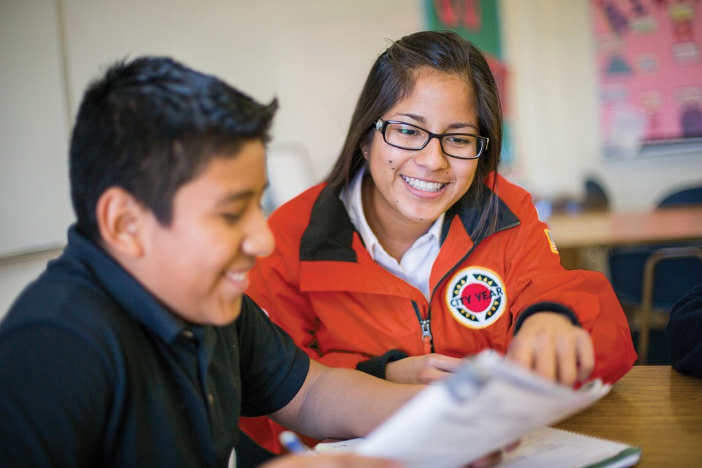 city year americorps member with a student sitting at a desk as they read together from the same paper