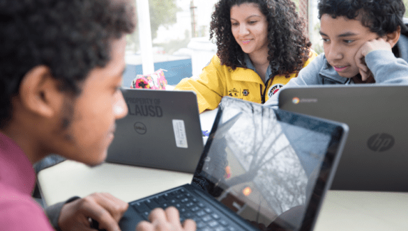 City Year AmeriCorps member and two students complete homework on laptop computers Comcast NBCUniversal partnership