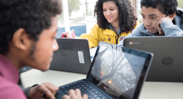 City Year AmeriCorps member and two students complete homework on laptop computers Comcast NBCUniversal partnership