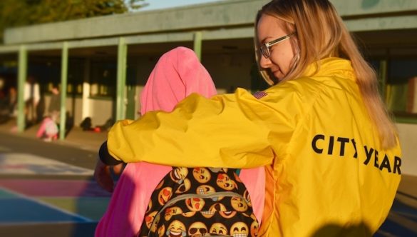 An AmeriCorps member waking into school with a student with an emoji backpack
