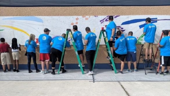 AT&T volunteers and students from the school paint the plywood mural. 