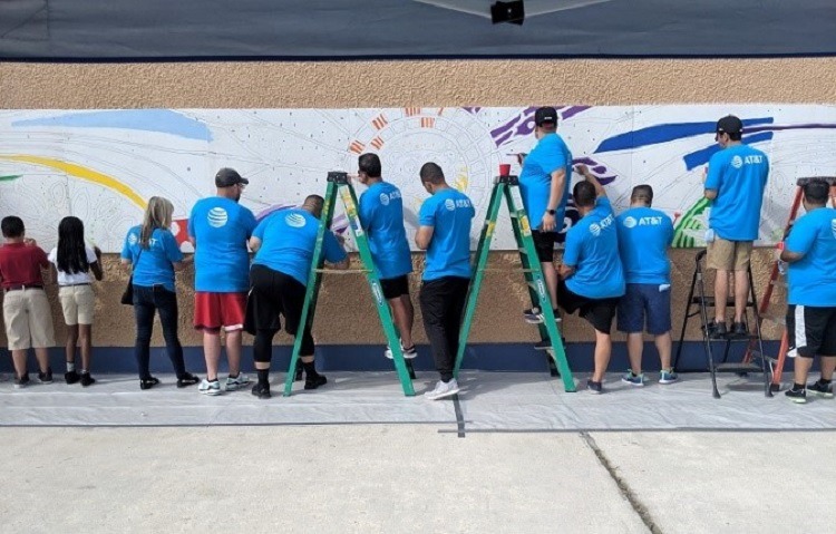 AT&T volunteers and students from the school paint the plywood mural. 