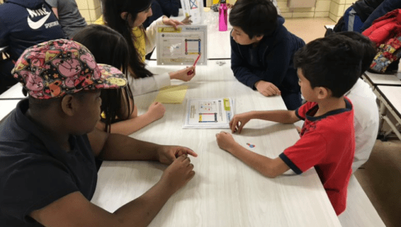 City Year AmeriCorps member points to a chart as four students gathered around a table look on