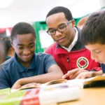 a middle school student smiles while reading with an AmeriCorps member