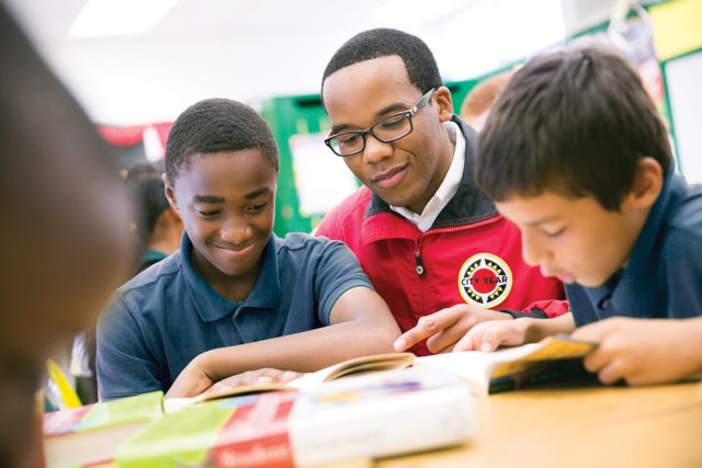 a middle school student smiles while reading with an AmeriCorps member