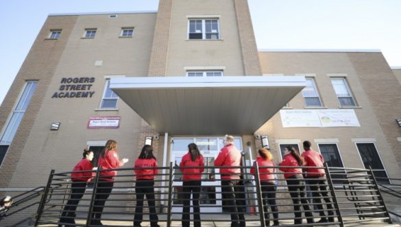 Nine City Year AmeriCorps members stand against an iron railing outside a brick school building