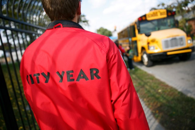 An AmeriCorps member watches students board school buses