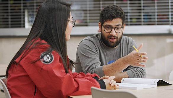 City Year AmeriCorps member chatting with a teacher while seated at a desk in front of a blackboard