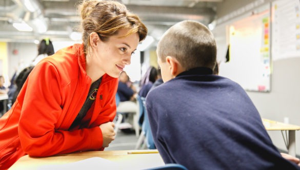 City Year Buffalo AmeriCorps member Bethany Elliot stands at a desk next to a student