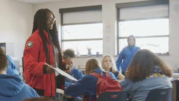 Smiling City Year AmeriCorp member standing in a classroom teaching seated students