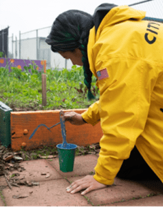 Corpsmember paints a flowerbed in a school garden