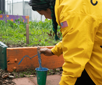 Corpsmember paints a flowerbed in a school garden