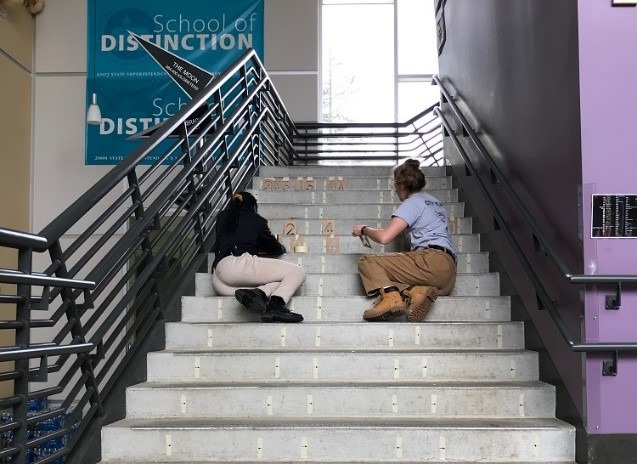 Two Care Force members sit on a set of stairs taping stencils to the risers.