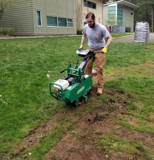 Care Force member using sod cutter on a large grassy area with a building in the background.