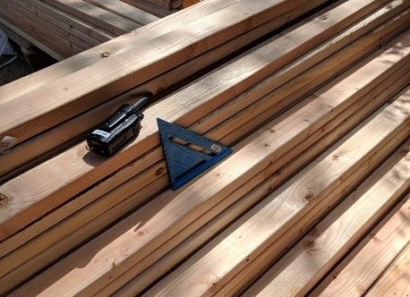 A walkie talkie and a carpenter square sit on several piles of lumber.