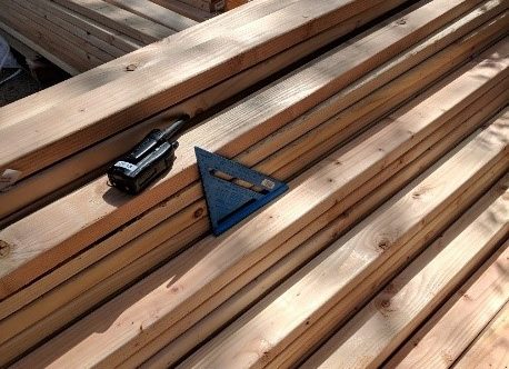 A walkie talkie and a carpenter square sit on several piles of lumber.