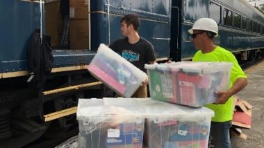 Two men loading plastic containers filled with toys onto the CSX Santa Train.