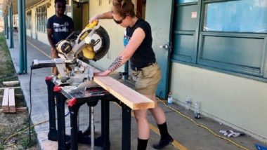 Two AmeriCorps Members use a chop saw on a saw horse to cut wood.