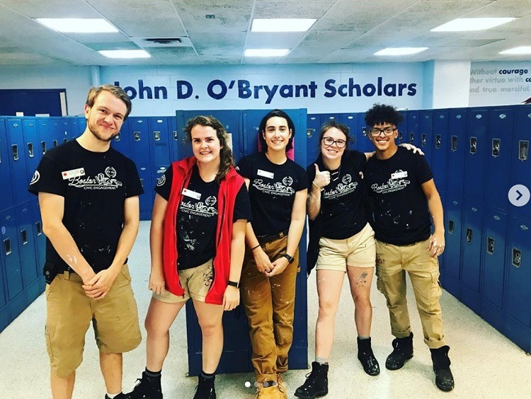 Four Senior AmeriCorps members and their Volunteer Impact Manager stand in front of blue lockers wearing black Boston City Year skyline shirts.