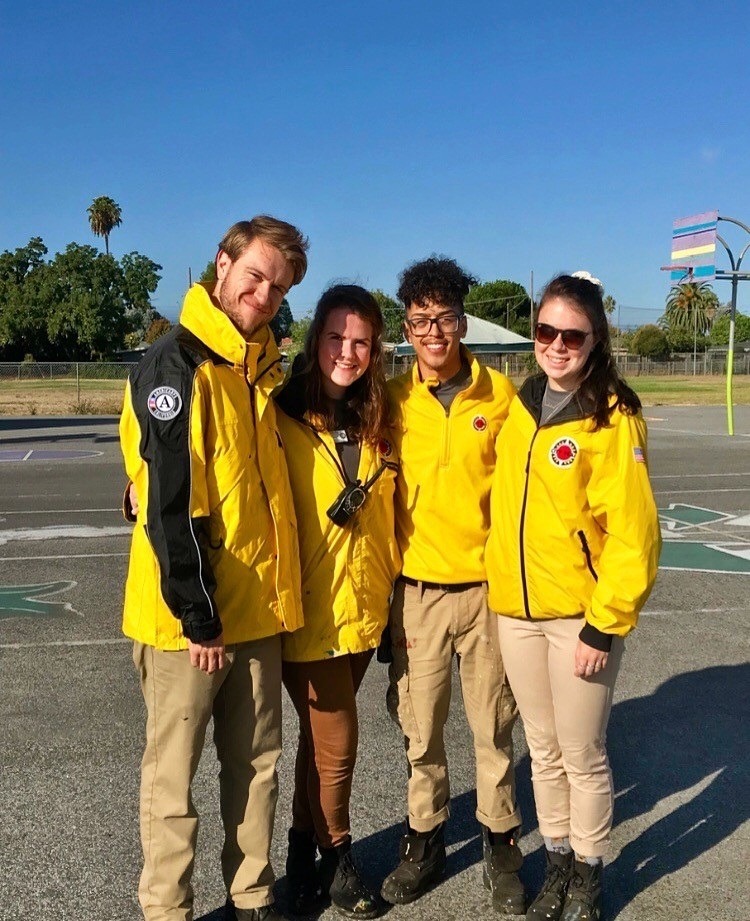 Four Senior AmeriCorps members stand on a blacktop with yellow City Year jackets, khakis, and black Timberlands.