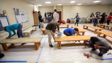 Volunteers stain backless benches on tarp covered floor.