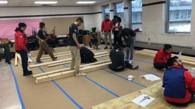 Volunteers stand in a room with piles of lumber for a construction project.