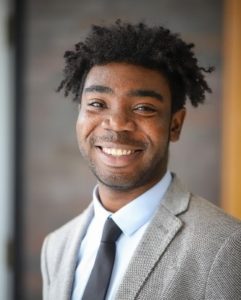 Headshot of Senior AmeriCorps Member Nana Boateng smiling in a grey jacket, white shirt, and black tie. 