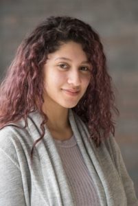 Headshot of Senior AmeriCorps Member Johanny Tejada smiling in a grey shirt with a grey cardigan. 