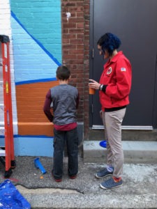 Abby Cozzolino paints a mural with a Parkside student