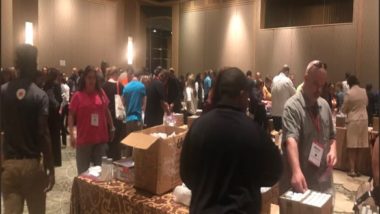 Aramark volunteers stand in a ballroom at various tables packing boxes.