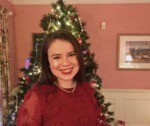 Senior AmeriCorps Member Claire Turner standing in front of a decorated Christmas tree wearing a red sweater and pearl necklace.
