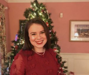 Senior AmeriCorps Member Claire Turner standing in front of a decorated Christmas tree wearing a red sweater and pearl necklace.