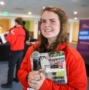 Senior AmeriCorps Member Halli Grunder holding a microphone and clipboard wearing the iconic City Year full zip jacket.