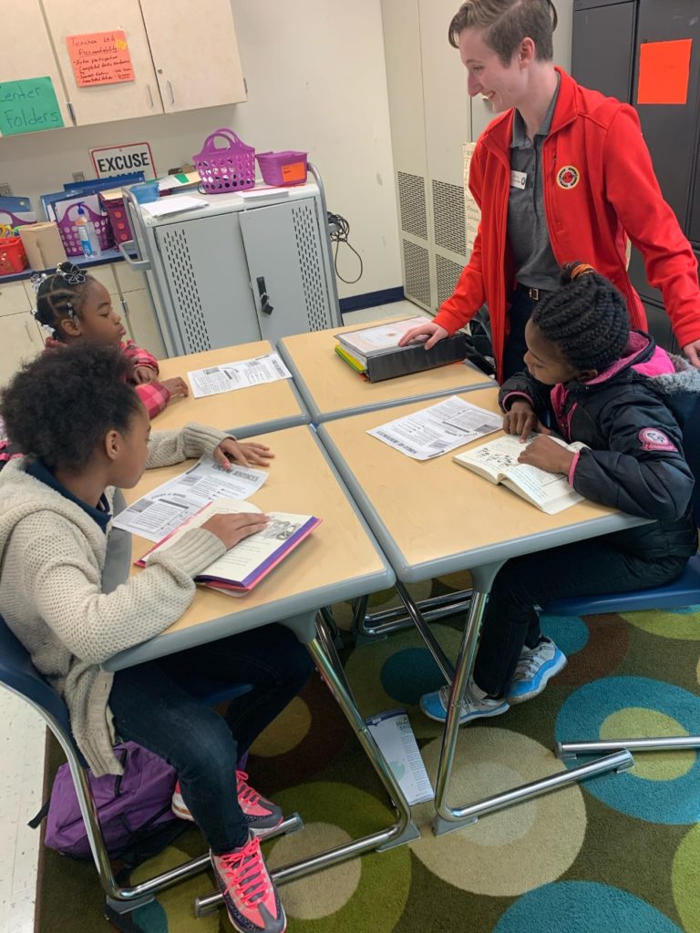 AmeriCorps member in red jacket mentors students with books open in Jacksonville, Florida.