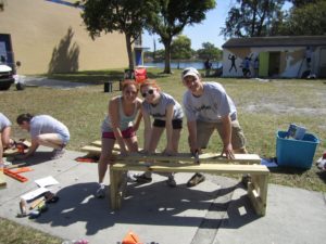 Three volunteers pose with backless bench they are building.