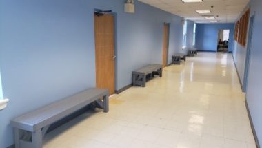 Hallway with blue walls and backless benches in the spaces between classrooms.