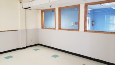 Photo of a finished room painting project with top half of the wall painted white and the bottom half painted light gray. There are three windows on the far walls with brown borders.