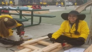 Two women in yellow jackets work on a construction project. 