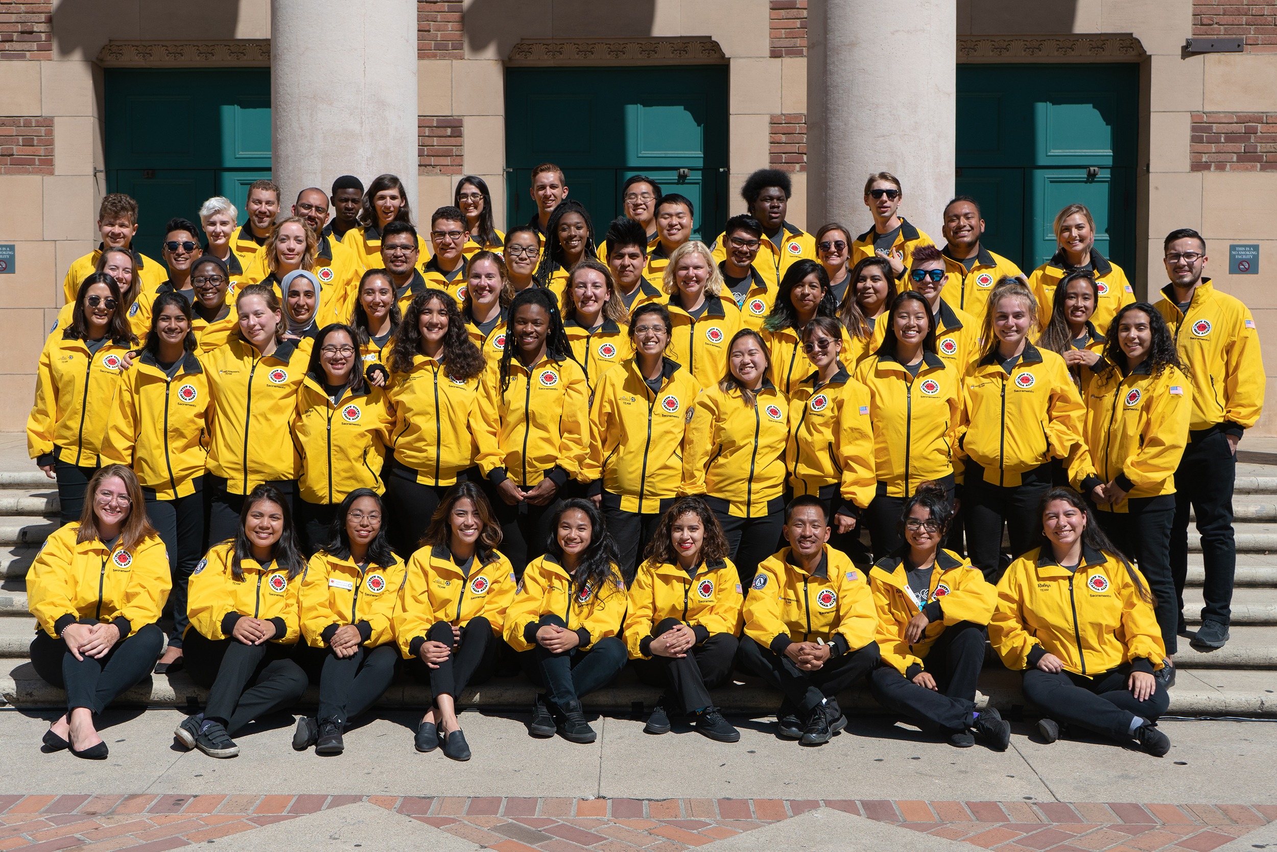 62 corps members wearing yellow jackets pose for the camera