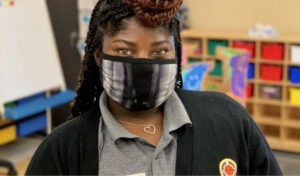 A City Year AmeriCorps member in a mask welcomes you to her elementary classroom