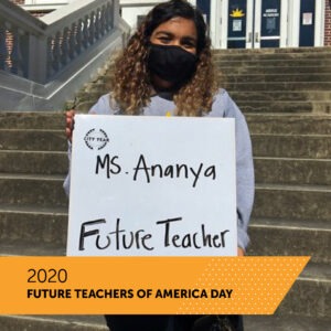 A City Year AmeriCorps member holds a board with her name Ms. Ananya and the title Future Teacher as she stands on the front steps of her school. There is a banner that reads 2020 Future Teachers of America Day.