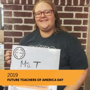 A City Year AmeriCorps member holds a board with her name Ms. T. There is a banner that reads 2019 Future Teachers of America Day.