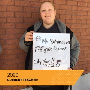 A City Year AmeriCorps member holds a board with her name Ms. Richardson, her title 7th-8th grade teacher and CIty Year New Orleans 2020l. There is a banner that reads 2020 Future Teachers of America Day.