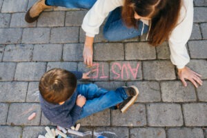 An aerial view of Amanda and her child writing on the sidewalk with chalk.